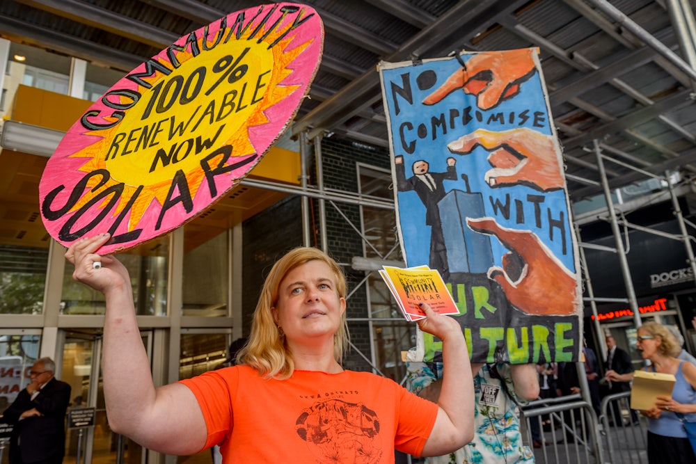 A demonstrator holds a sign reading "Community Solar: 100% Renewable Now."