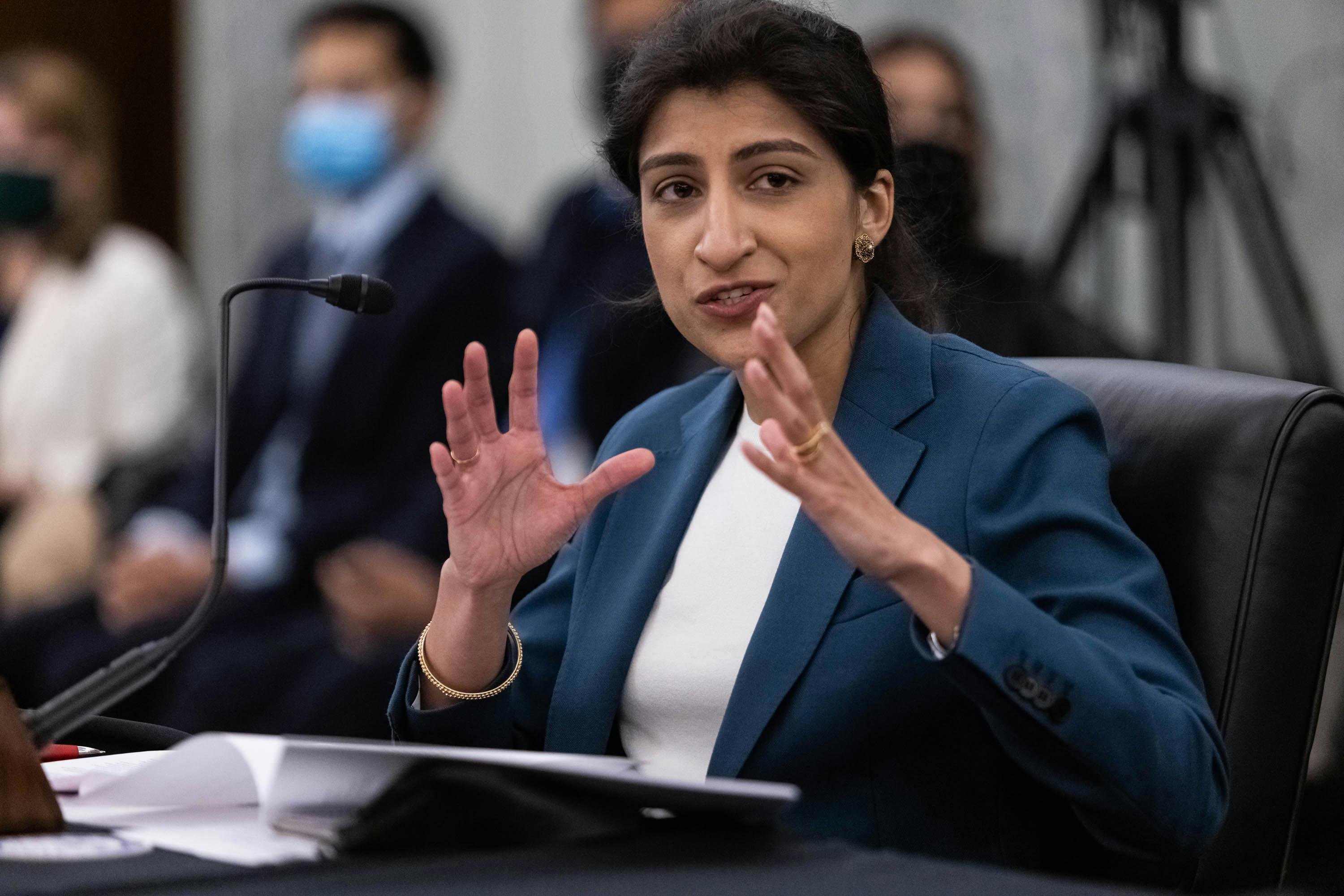 FTC Commissioner Lina M. Khan smiles and gestures with her hands while testifying during a Senate hearing 