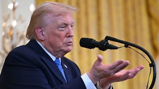 Donald Trump makes a hand gesture while he stands at a podium.