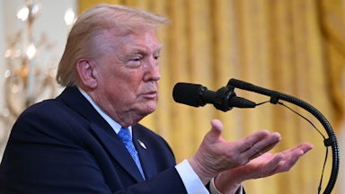 Donald Trump makes a hand gesture while he stands at a podium.