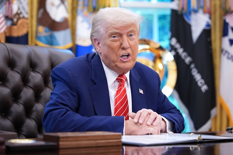 Donald Trump speaks while seated at his desk in the Oval Office of the White House. It almost seems like he's snarling.