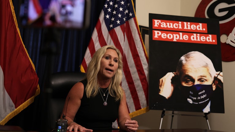 Marjorie Taylor Greene speaks to reporters next to a sign denigrating Dr. Anthony Fauci.