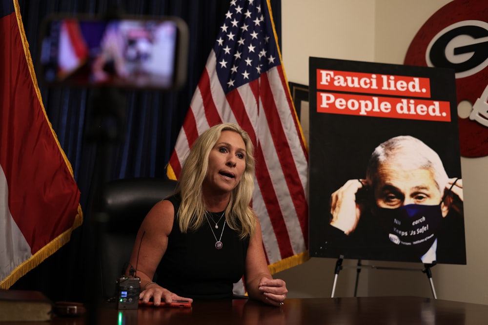 Marjorie Taylor Greene speaks to reporters next to a sign denigrating Dr. Anthony Fauci.