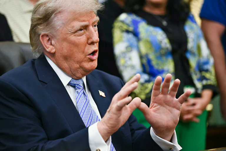 Donald Trump gestures and speaks while sitting at his desk in the Oval Office