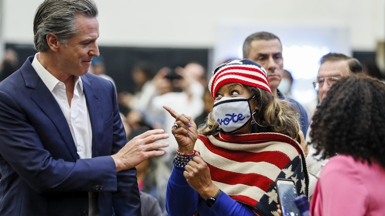 Gavin Newsom passes a woman clad in an American flag scarf, with a mask reading "vote."