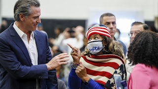 Gavin Newsom passes a woman clad in an American flag scarf, with a mask reading "vote."