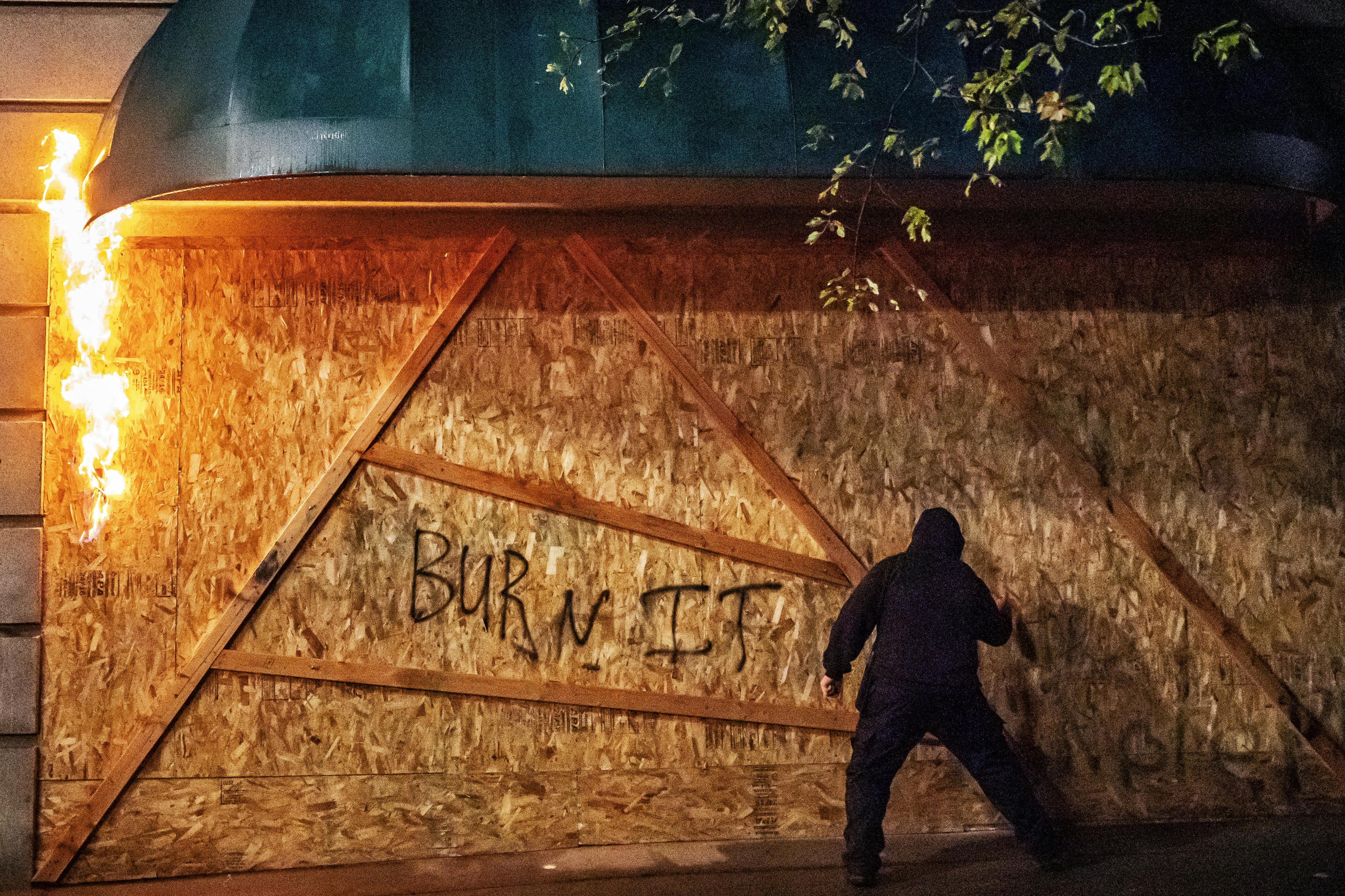 An anti-police protester sprays graffiti on the side of a burning plywood barrier at the Multnomah County Justice Center in Portland.