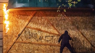 An anti-police protester sprays graffiti on the side of a burning plywood barrier at the Multnomah County Justice Center in Portland.