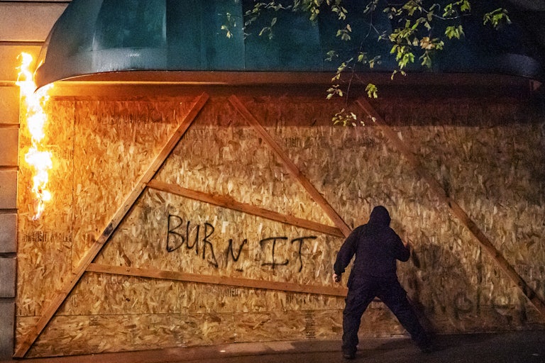An anti-police protester sprays graffiti on the side of a burning plywood barrier at the Multnomah County Justice Center in Portland.