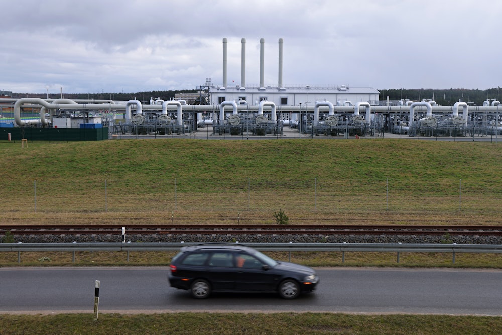A car drives in front of a series of pipes and gears.
