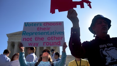 Demonstrators hold a cut out of a gerrymandered district in front of the Supreme Court.