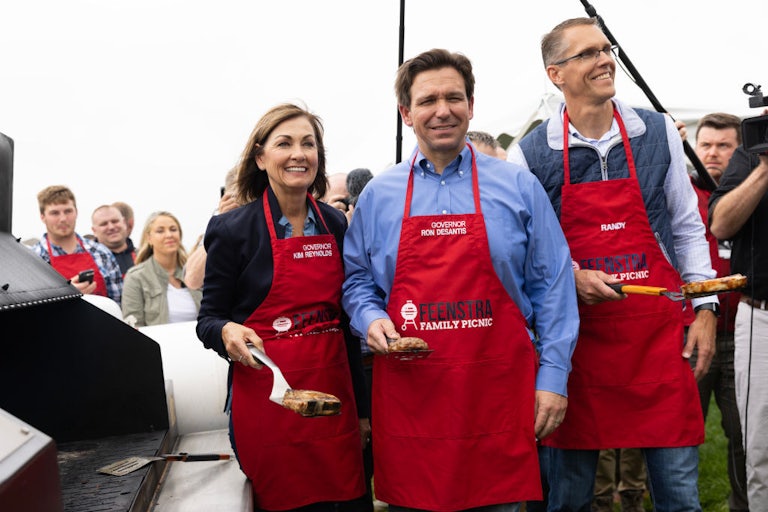 Reynolds, DeSantis, and Feenstra pose holding spatulas and meat while wearing red aprons.