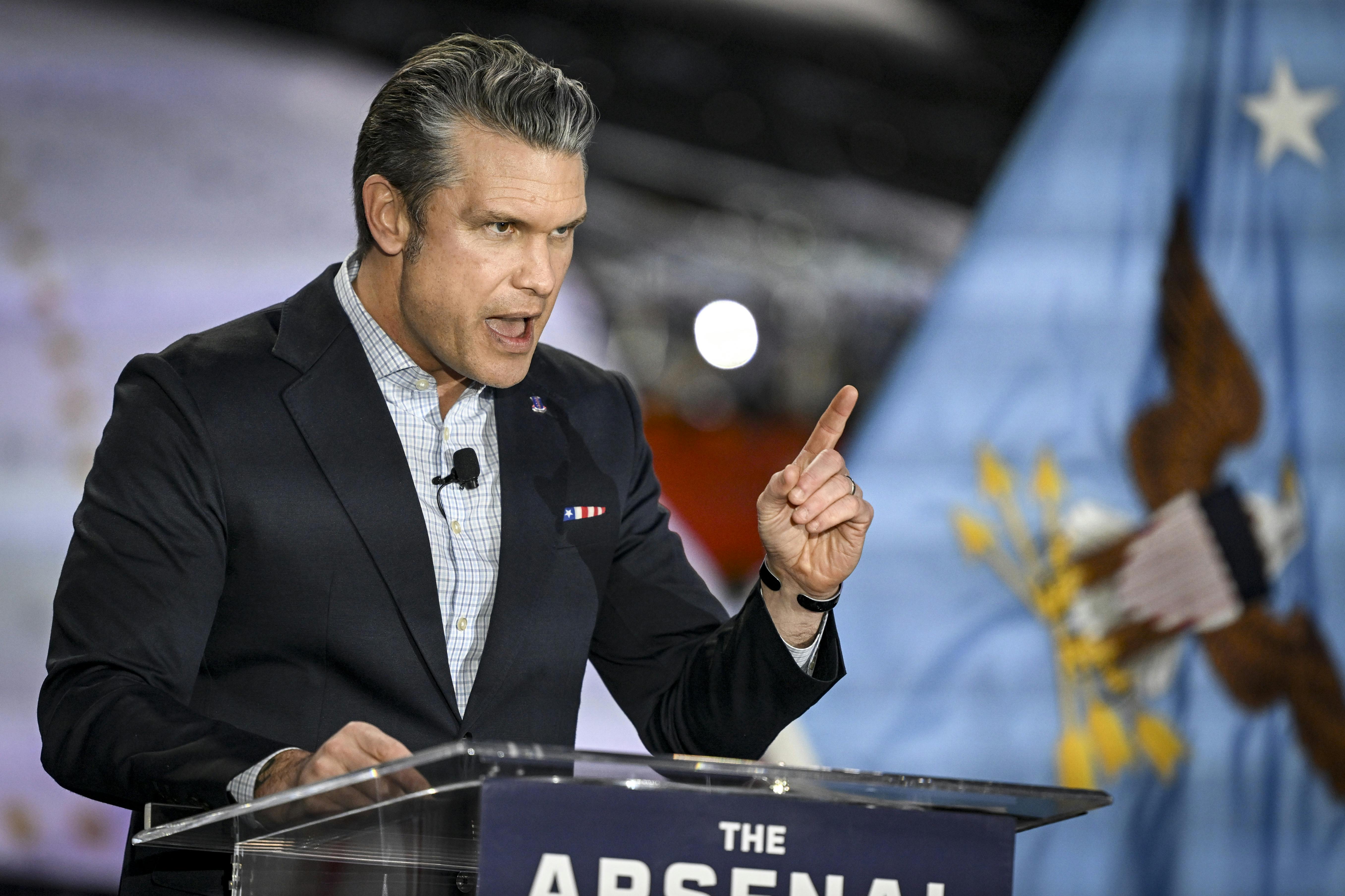Defense Secretary Pete Hegseth speaks at a lectern whlie pointing and hunching over slightly.