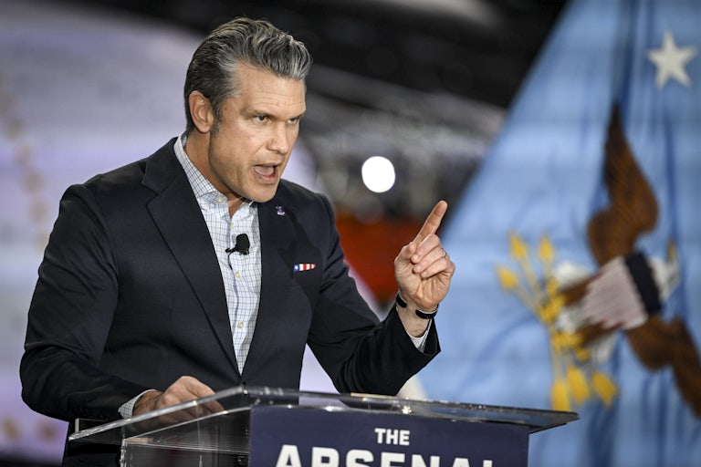 Defense Secretary Pete Hegseth speaks at a lectern whlie pointing and hunching over slightly.