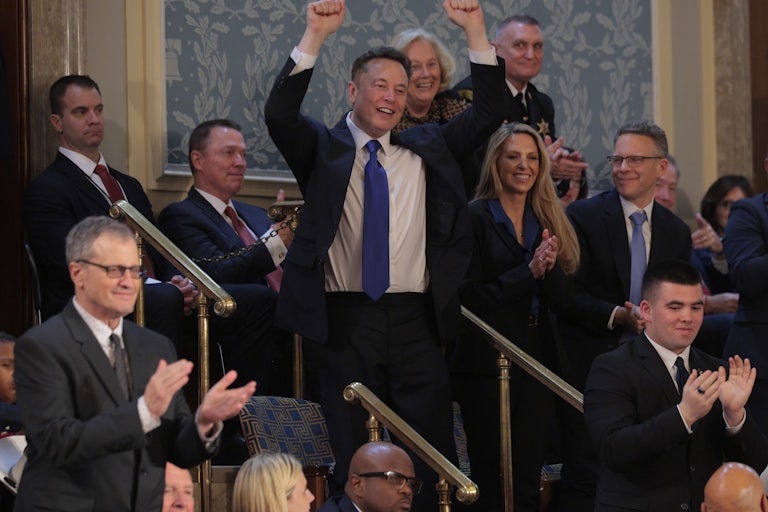 Elon Musk holds his arms above his head while standing in the gallery during Donald Trump’s address to Congress