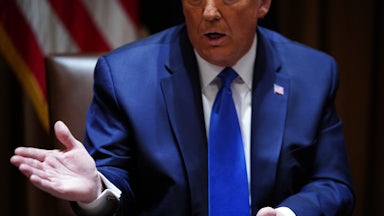 Donald Trump, sitting at a desk, gestures while he speaks