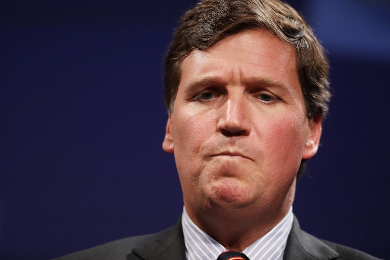 A man wearing a suit and red tie looks down and scrunches up his face in confusion