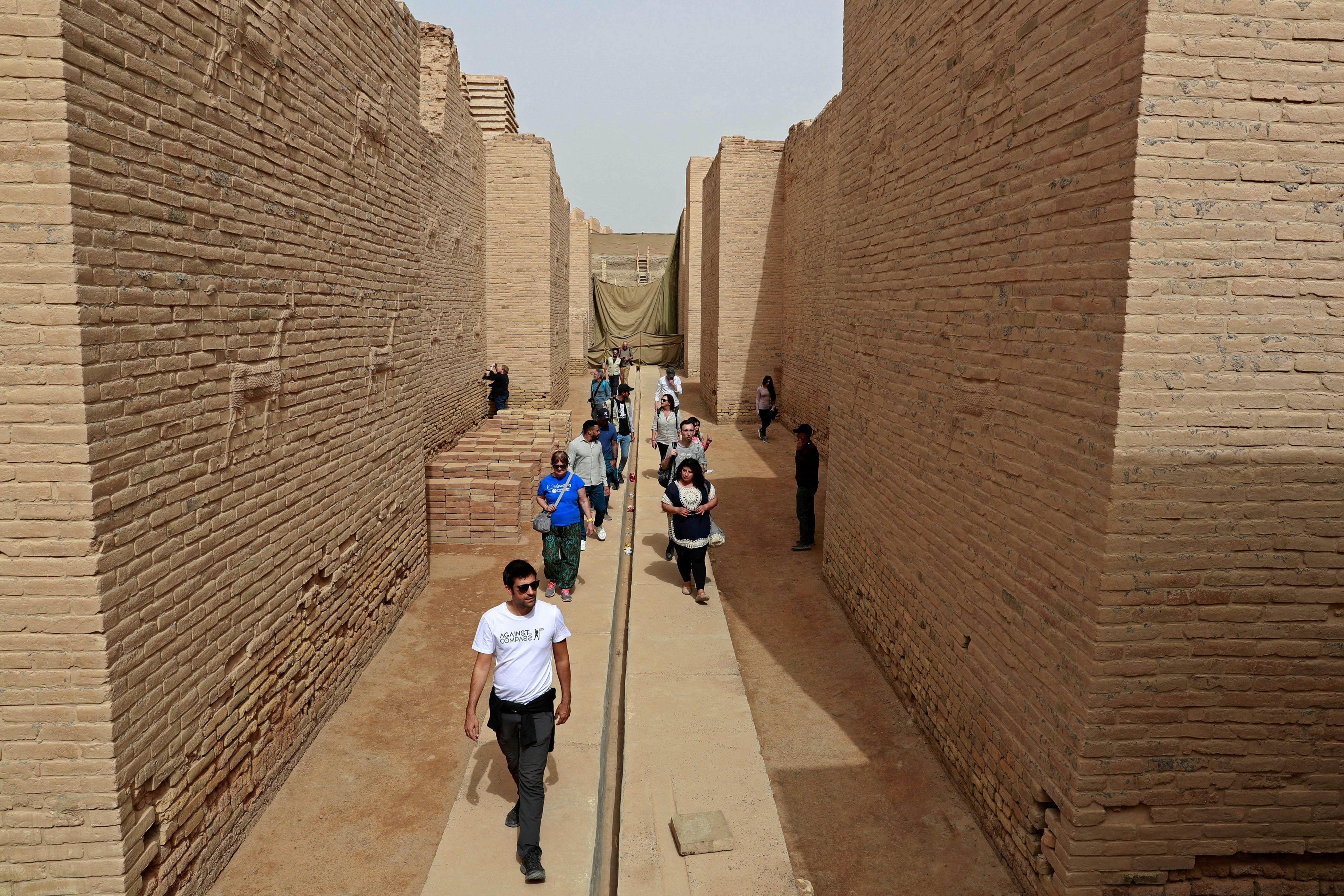 Tourists walk between high stone walls.
