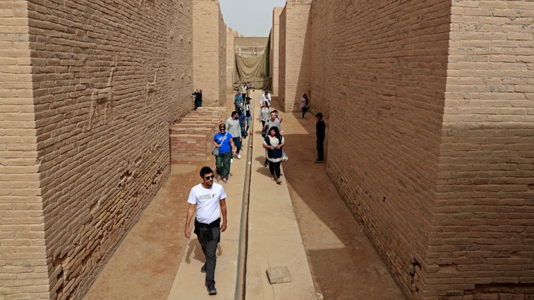 Tourists walk between high stone walls.