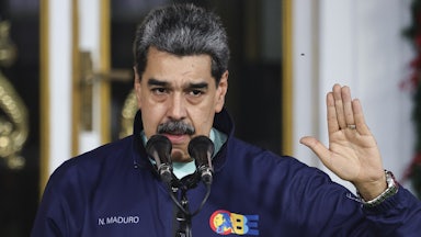 Venezuela's Nicolas Maduro speaks into a mic while putting a hand up as if making a pledge.