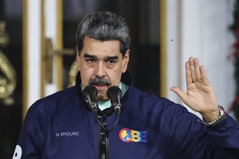 Venezuela's Nicolas Maduro speaks into a mic while putting a hand up as if making a pledge.