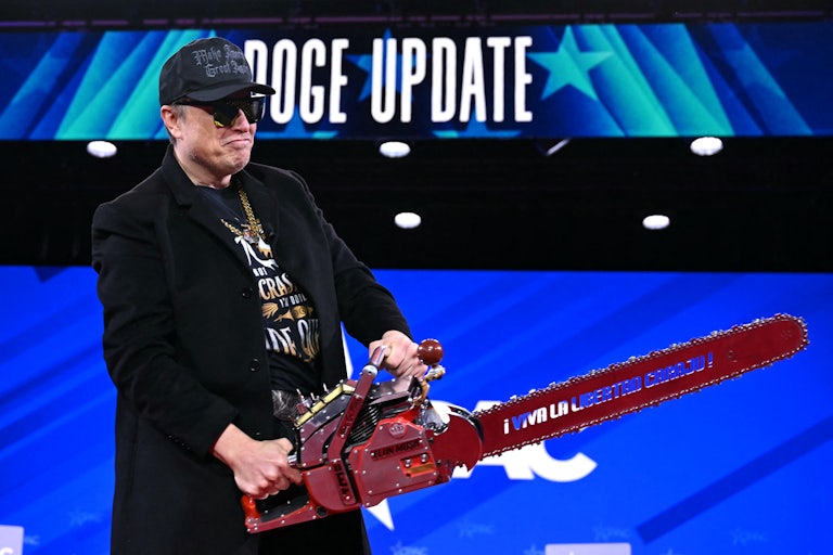 Elon Musk wears sunglasses and a black MAGA hat and holds a chainsaw on the CPAC stage. Behind him, a screen reads "DOGE Update."