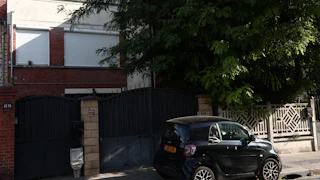 A small car parked in front of a gated home