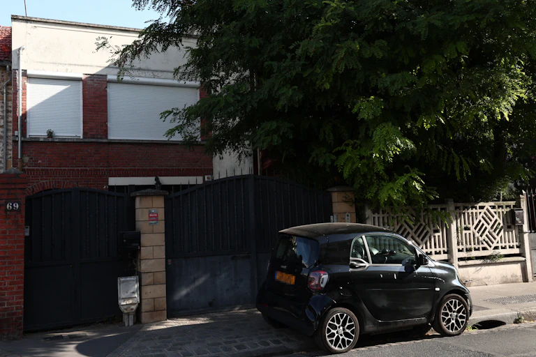 A small car parked in front of a gated home