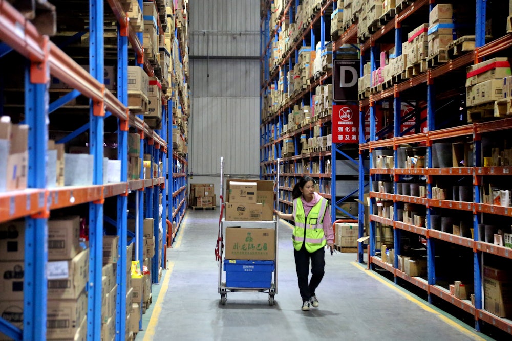 A young woman walks through a warehouse with a cart of stock.