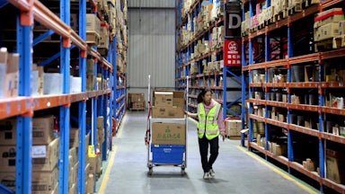 A young woman walks through a warehouse with a cart of stock.