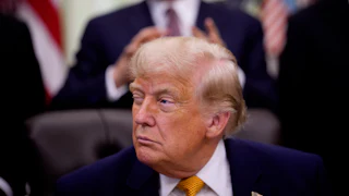 Trump squints with one eye open as he sits at his desk in the Oval Office of the White House