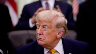 Trump squints with one eye open as he sits at his desk in the Oval Office of the White House