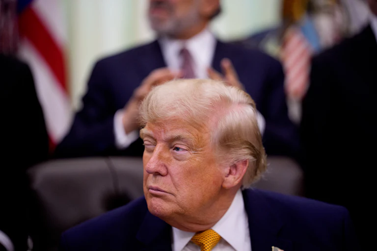 Trump squints with one eye open as he sits at his desk in the Oval Office of the White House