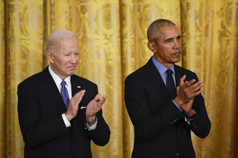 Joe Biden and Barack Obama clap, standing side by side. Obama looks grim.