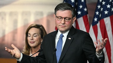 House Speaker Mike Johnson shrugs while standing at a podium