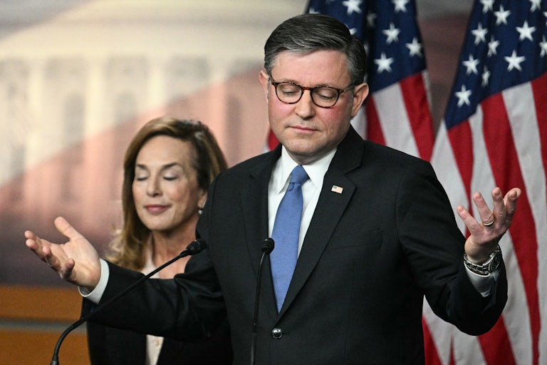 House Speaker Mike Johnson shrugs while standing at a podium