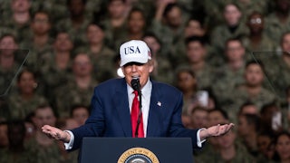 Donald Trump wearing a USA cap shrugs his arms as he speaks to U.S. troops.