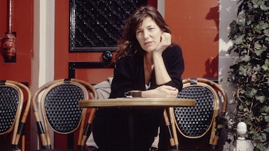 Jane Birkin at an outdoor café in Paris sitting at a bistro table with her dog at her feet