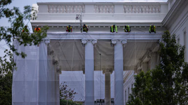 Workers hang a tarp printed with the North Portico on the White House