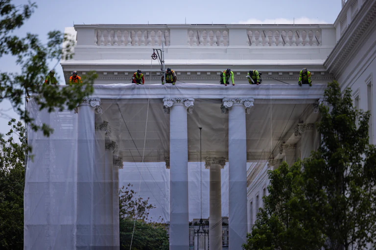 Workers hang a tarp printed with the North Portico on the White House
