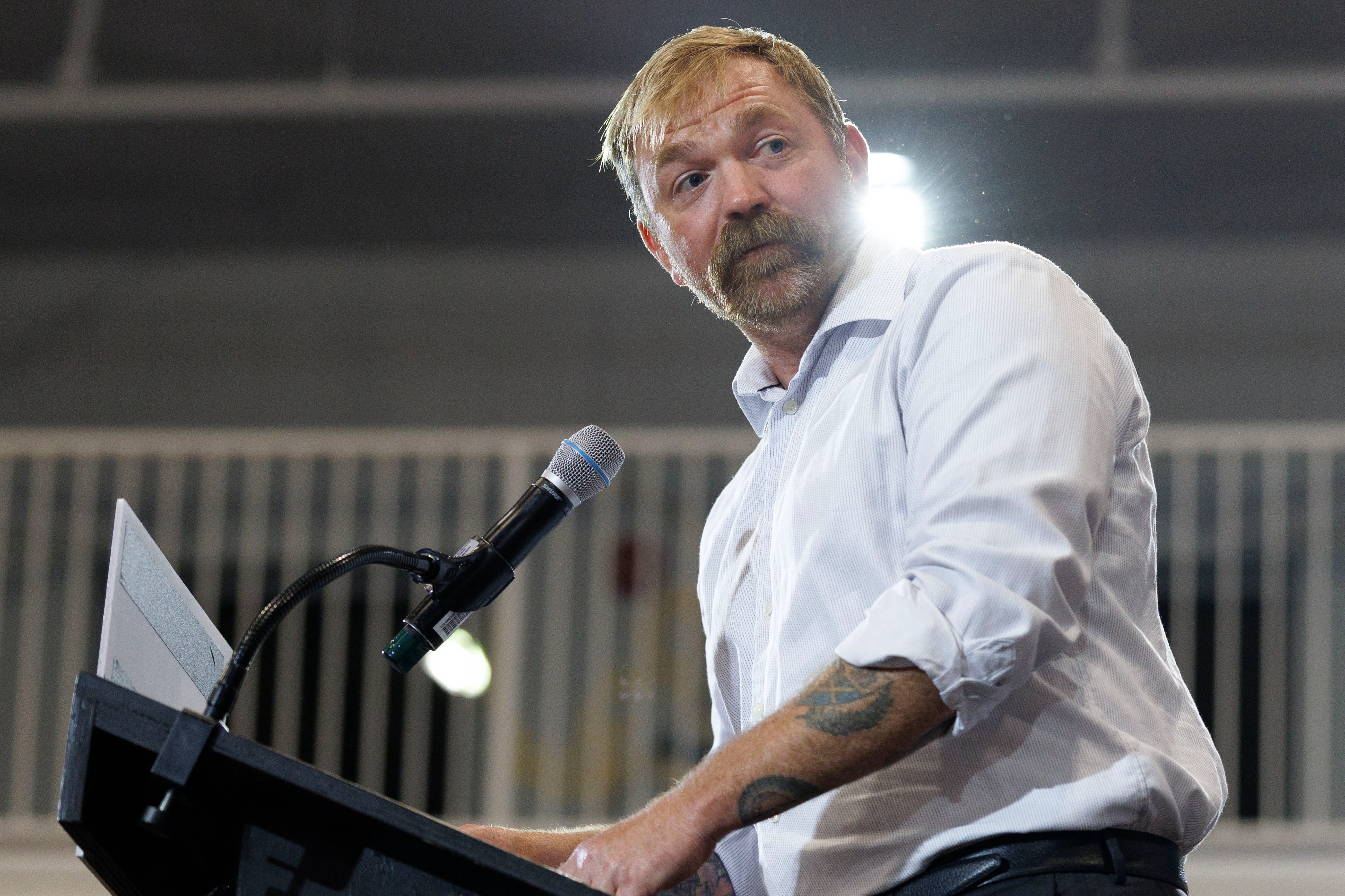 Democratic U.S. Senate candidate Graham Platner stands at a podium, his sleeves rolled up to show his tattoos.