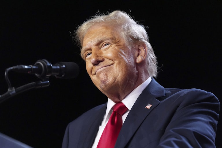 Donald Trump smiles while standing in front of a microphone