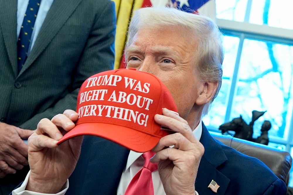 Donald Trump holds a red hat in front of his face. The hat says "TRUMP WAS RIGHT ABOUT EVERYTHING!"