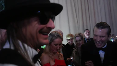 Pete Hegseth bends over at the waist as he laughs at Kid Rock. Hegseth's wife smiles in the background.