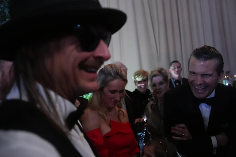 Pete Hegseth bends over at the waist as he laughs at Kid Rock. Hegseth's wife smiles in the background.