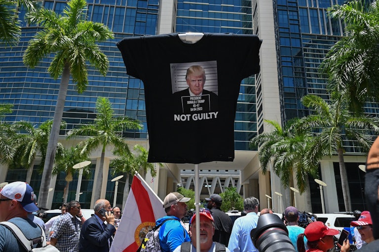 A man holds up a stick with a t-shirt attached to the top that says NOT GUILTY under a photo of Trump.