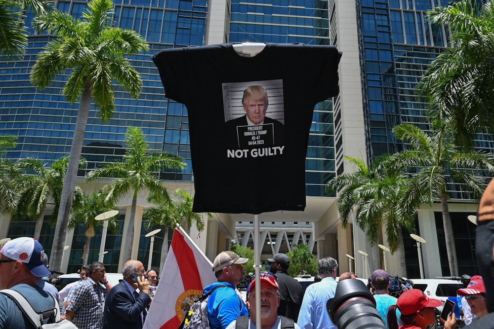 A man holds up a stick with a t-shirt attached to the top that says NOT GUILTY under a photo of Trump.