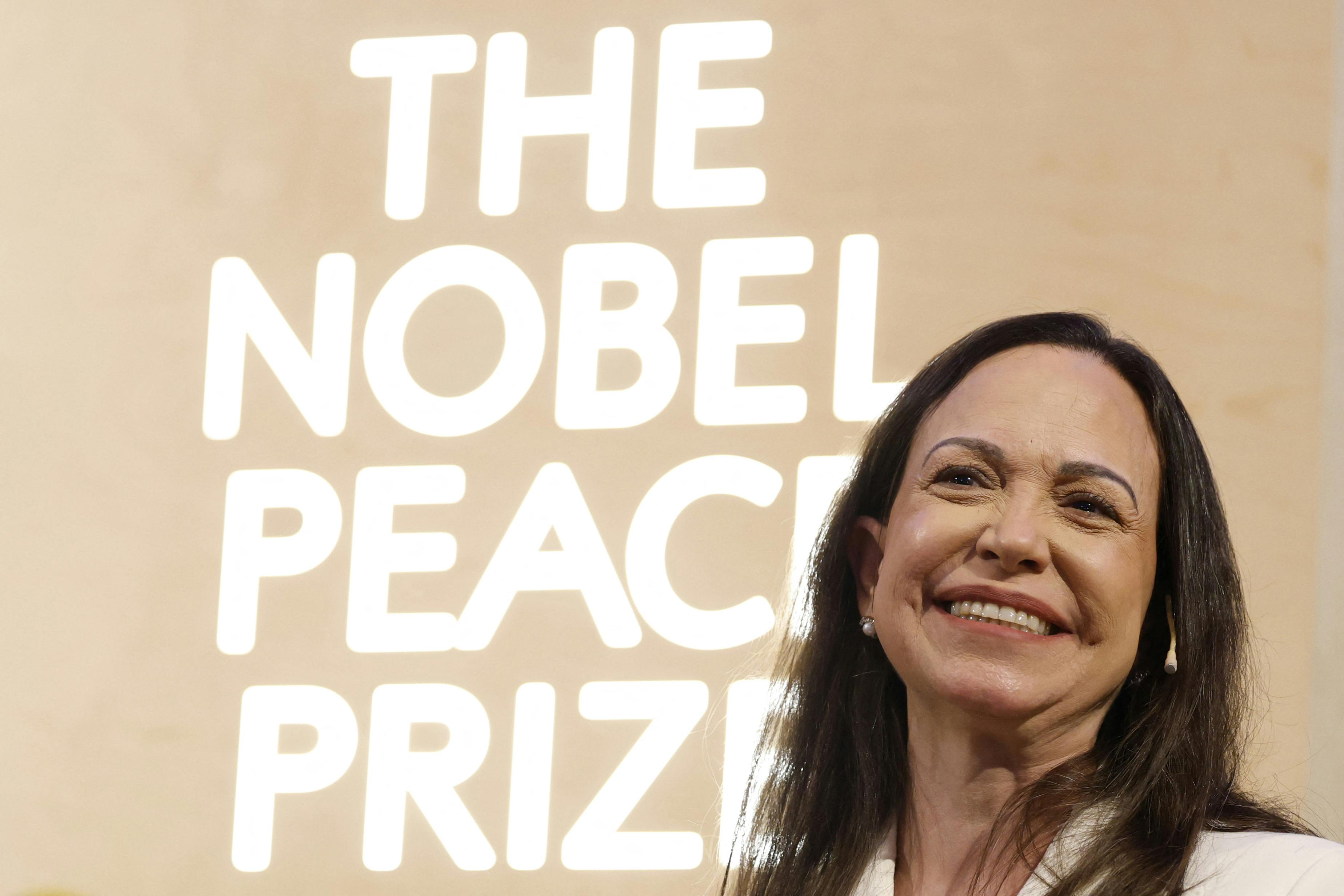 Venezuelan opposition leader Maria Corina Machado smiles in front of a backdrop that says, "The Nobel Peace Prize"