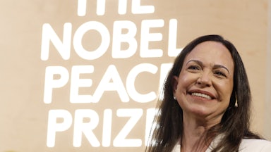 Venezuelan opposition leader Maria Corina Machado smiles in front of a backdrop that says, "The Nobel Peace Prize"