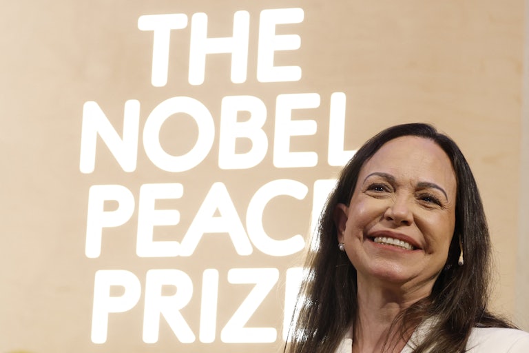 Venezuelan opposition leader Maria Corina Machado smiles in front of a backdrop that says, "The Nobel Peace Prize"